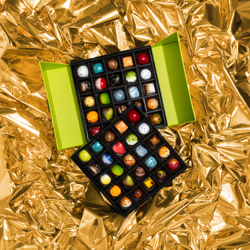 A stunning green tiered gift box featuring all 10 limited-edition holiday chocolates alongside 40 pieces from our signature collection. The gift box is nestled in gold paper. 